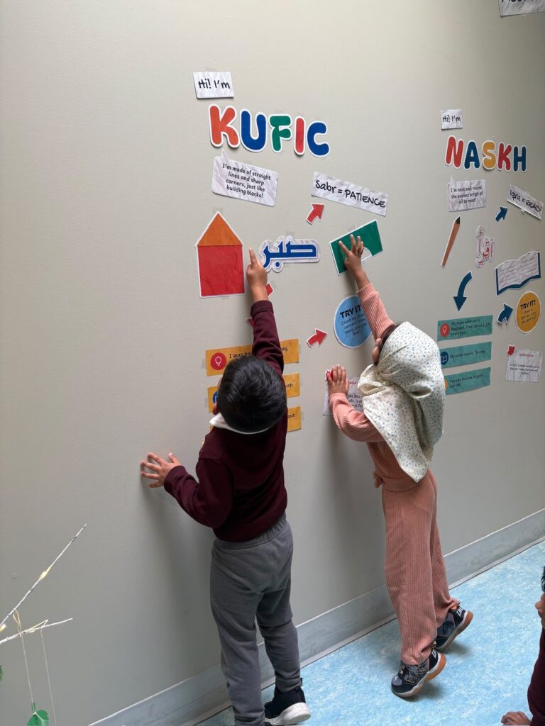 Two students reaching up to the Kufic column during their visit